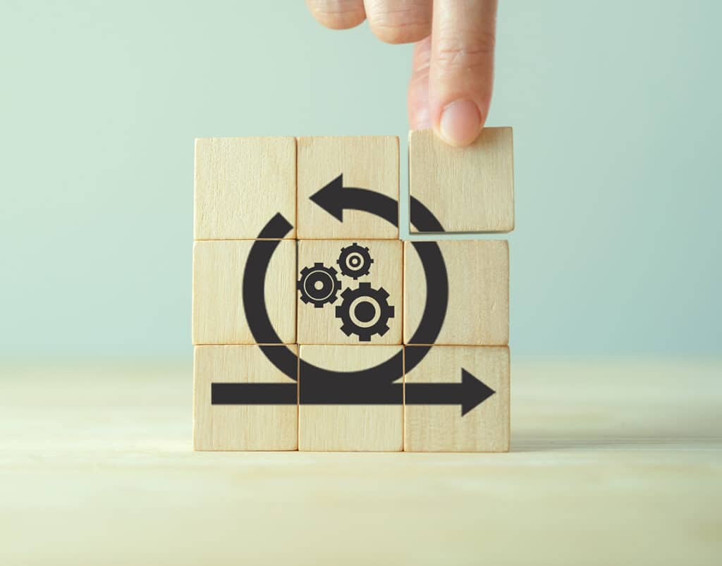 Main assemblant des cubes en bois pour former le logo de la méthode Agile, illustrant l'approche de notre agence pour la création de site web.